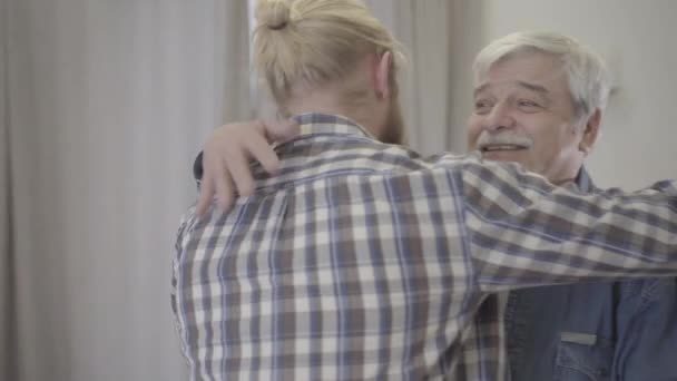 Närbild av glad äldre kaukasisk man kramar vuxen son inomhus. Porträtt av leende seniorpensionär glad över mötet. Familj, livsstil, enhet, lycka. — Stockvideo