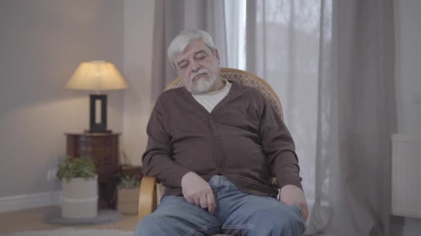 Adult male nurse covering sleeping retiree with blanket and leaving. Portrait of senior grey-haired man resting in armchair in nursing home. Care, help, support, lifestyle. — Stock Video