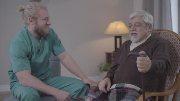 Вид сбоку положительный медбрат и пенсионер разговаривают и смеются. Взрослые белые и зрелые мужчины проводят счастливый вечер в доме престарелых. Радость, отдых, счастье . — стоковое видео