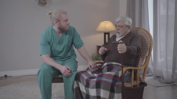 Mellanslag av gammal kaukasisk man dela med vuxna manliga sjuksköterska. Ung kille tar hand om klok senior pensionär. Livsstil, stöd, assistans, vårdhem. — Stockvideo