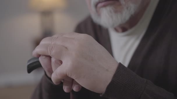 Extreme close-up van volwassen blanke handen met wandelstok. Onherkenbare oudere man met grijze baard die binnen denkt. Veroudering, levensstijl, pensionering, pensioen. — Stockvideo