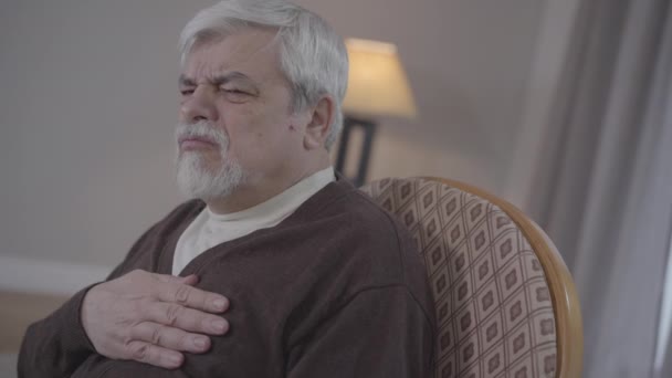 Vista lateral do velho homem caucasiano com dor súbita aguda no peito e chamando de emergência. O retrato do aposentado masculino sênior com doença cardiovascular precisa da ajuda de trabalhadores médicos. Doença, medicina . — Vídeo de Stock