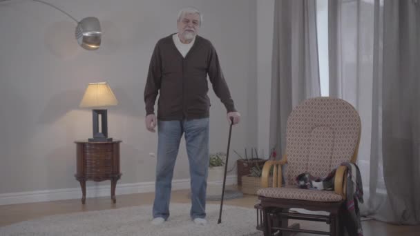 Retrato del viejo hombre caucásico con bastón de andar haciendo el gesto de escuchar música en casa. Amplio tiro de jubilado senior positivo disfrutando de la noche en el interior. Estilo de vida, alegría, afición, felicidad . — Vídeo de stock