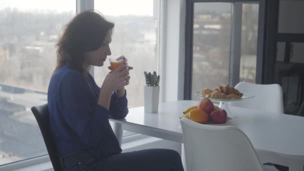 Pandangan samping dari wanita kaukasia yang percaya diri berbau jus jeruk dan mengambil buah. Pengusaha kaya yang sarapan sendirian di rumah. Kesepian, kesedihan, gaya hidup . — Stok Video