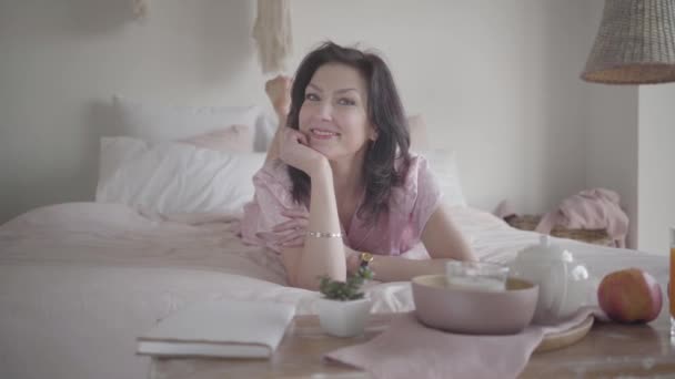 Portrait de magnifique femme blanche adulte couchée sur le lit le matin et souriante. Brunette dame confiante profiter des week-ends à la maison. Mode de vie, loisirs, joie, repos . — Video