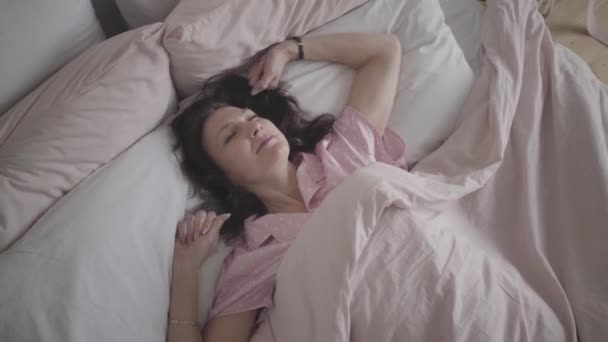 Vue du dessus de la femme blanche adulte positive s'étendant dans le lit le matin et souriant à la caméra. Portrait de dame brune heureuse se réveillant dans la chambre. Loisirs, mode de vie, détente . — Video