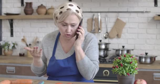 Mujer caucásica estresada de ojos marrones hablando por teléfono y colgando. Retrato de una jubilada irritada pasando la noche sola en la cocina en el interior. Estilo de vida, soledad. Sede del cine 4k ProRes . — Vídeos de Stock