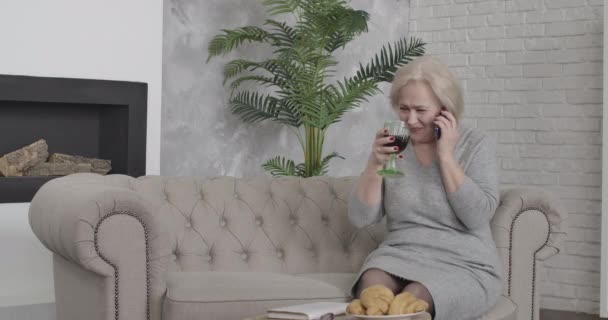 Portrait of joyful middle-aged Caucasian woman laughing and talking on the phone. Confident happy retiree drinking red wine and chatting with friend. Happiness, joy, lifestyle. Cinema 4k ProRes HQ. — Stock Video