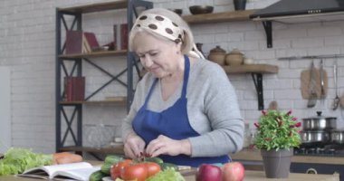 Beyaz bir kadının salata için salatalık keserken ve bir dilim salatalık yerken yan görüntüsü. İçeride gülümseyen ve organik sebze yiyen olgun bir kadının portresi. Yemek pişirmek. Sinema 4k ProRes Merkezi.