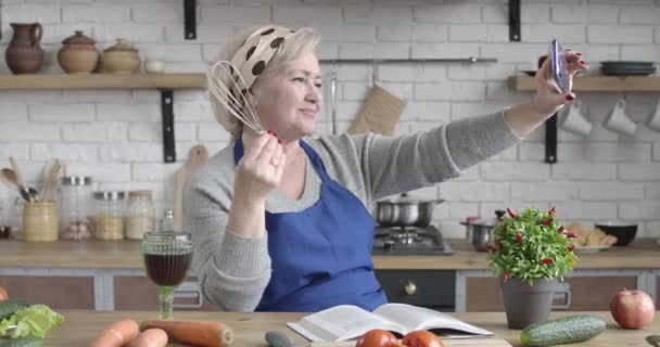 Moderne oudere blanke vrouw neemt selfies met kookgerei in de keuken. Portret van vrolijke vrouwelijke gepensioneerde poseren met garde binnen. Lifestyle, vreugde, pensioen. Cinema 4k ProRes Hoofdkwartier. — Stockvideo