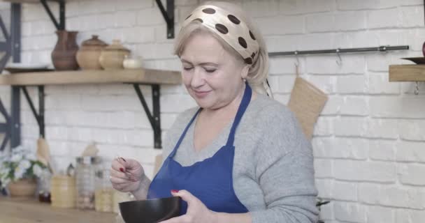 中年白人女人在碗里打打配料，对着相机笑。正退休人员在现代厨房准备食物的画像。生活方式，烘焙，烹调。Cinema 4k ProRes HQ. — 图库视频影像