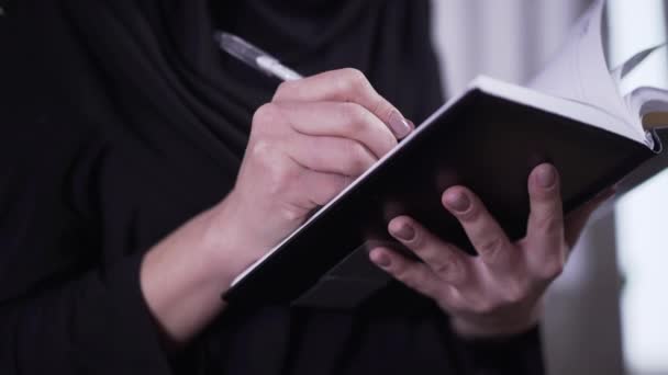 Primo piano delle mani femminili che scrivono un libro. Donna musulmana irriconoscibile in abito tradizionale e scrittura hijab a casa. Letteratura, creatività, stile di vita . — Video Stock