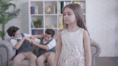 Kamera, beyaz, şirin bir kıza yaklaşıyor. Geriye dönüp ikiz kardeşlerin kavga edişine bakıyor. Kameraya dönüp gülümsüyor. Arka planda oynayan çocuklar gibi içeride poz veren güzel bir çocuk. Yaşam biçimi.