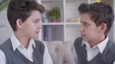 Birbirlerine bakıp gülümseyen tek yumurta ikizlerinin yakın plan görüntüsü. Havalı esmer, beyaz erkekler, aynı şık kıyafetleri giyip kapalı mekanda poz veriyorlar. Mutluluk, birlik, yaşam tarzı.