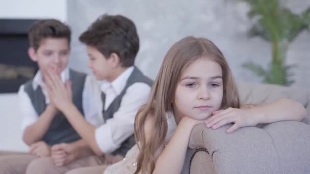 Meninos gêmeos desfocados dando alta cinco e brincando com o cabelo da menina triste bonito. Irmã perturbada olhando para eles para deixá-la sozinha, virando-se para a câmera. Foco muda de primeiro plano para trás e para trás . — Vídeo de Stock