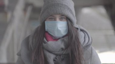 S-log 2. Kışlık giysiler içindeki esmer gri gözlü kız portresi ve kameraya bakan koruyucu maske. Karantina sırasında dışarıda poz veren beyaz bir kadın. Sağlık, güvenlik, yaşam tarzı, izolasyon