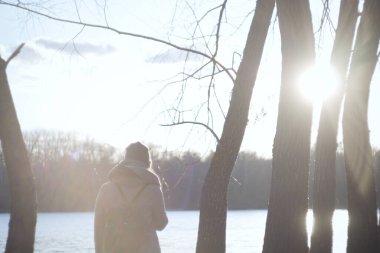 Gölün kıyısında gün ışığında tanınmayan bir kadın. Sıcak elbiseli bir kızın parkta dinlendiği arka plan görüntüsü. Yaşam tarzı, güzellik, doğa..