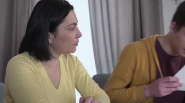 Genç beyaz bir kadının çayını içmesi, genç bir çocuktan kötü haber alıyormuş gibi görünüyor. Esmer anne akademik dışlanma ve şarkı söyleme ile ilgili belgelere bakıyor. Eğitim, tembellik.