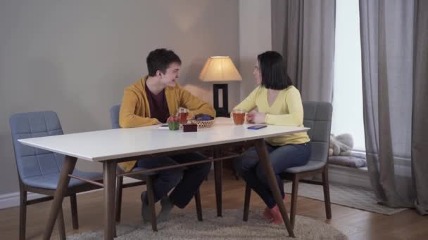 Long plan de heureux fils adolescent caucasien et mère adulte assis à la table et parlant. Femme et garçon souriants se reposant à l'intérieur. Mode de vie, loisirs, unité, communication . — Video