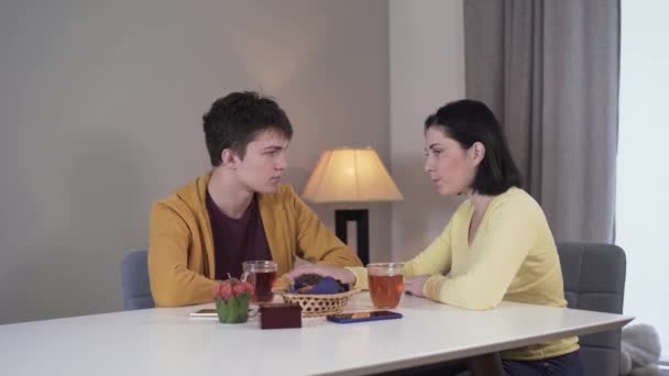 Plan médian d'une femme brune caucasienne anxieuse annonçant de mauvaises nouvelles à un adolescent. Mère partageant des problèmes avec son fils assis à la table à l'intérieur. Mode de vie, unité, confiance, famille . — Video