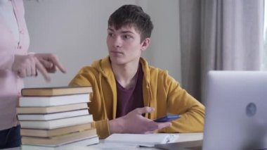 Öğrenmek yerine telefonu kullanan tembel beyaz erkek üniversite öğrencisinin portresi. Tanımlanamayan anne cihazı alıp kitap yığınında gösteriyor. Eğitim almayı reddeden bir genç..