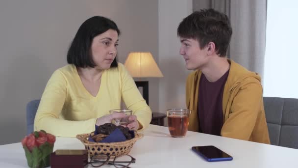 Brunette Kaukasische jonge vrouw geeft geld aan tienerzoon. Dankbare jongen die mam op de wang kust en weggaat. Eenheid, levensstijl, familie. — Stockvideo