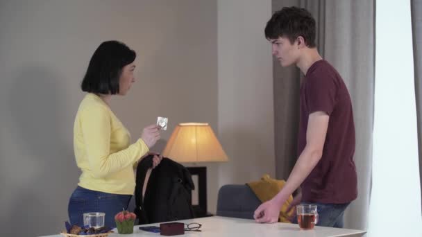 Zijaanzicht van blanke moeder en zoon die thuis ruziën. Vrouw toont condoom gevonden in jongens rugzak, tiener rechtvaardigt zichzelf. Probleem, familie, conflict, zorgen. — Stockvideo