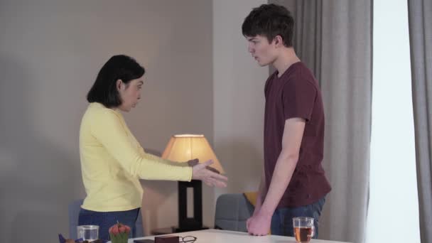 Side view of adult Caucasian woman and teenage boy arguing and gesturing emotionally indoors. Son and mother quarrelling at home. Conflict, misunderstanding, adolescence, motherhood. — Stock Video