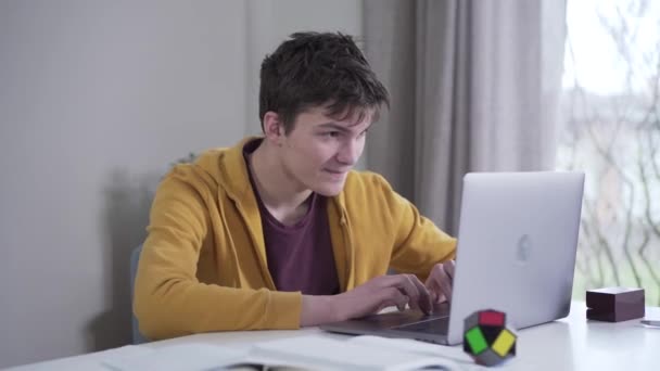 Porträt eines fröhlichen kaukasischen Teenagers, der Spiele auf dem Laptop spielt. Der junge Teenager ruht sich im Haus aus. Lebensstil, Glück, Spiel, Freizeit. — Stockvideo