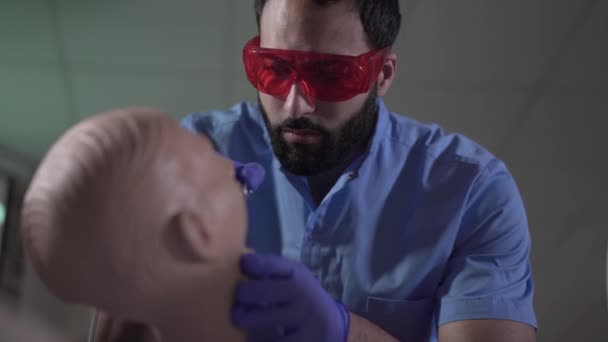 Närbild av koncentrerad Mellanöstern manlig stomatolog praktiserar med dentala skyltdocka. Självsäker stilig läkare förbättrar kvalifikationen. Medicin, livsstil, tandvård, yrke. — Stockvideo