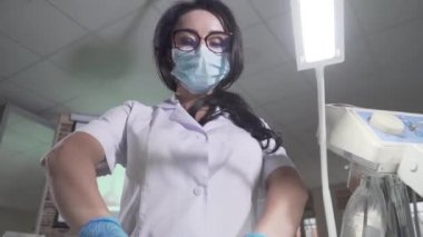 Genç, profesyonel kadın stomatolojistin diş aletleriyle kameraya yaklaşması. Esmer beyaz kadının portresi. Manipülasyon için ekipman kullanıyor. Diş hekimliği, odontoloji.