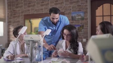 Orta Doğulu bir adam ve beyaz bir kadının diş kalıbından bahsederken ön planda. Öğretmen ve öğrenci dişçiliği tartışıyorlar. Eğitim, yaşam tarzı, odontoloji, tıp.