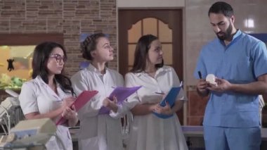Kafkasyalı ve Orta Doğulu diş hekimlerinin konuşmalarının ortası. Dişleri olan ve kadın asistanlara ders veren profesyonel bir erkek öğretim görevlisi. Odontoloji, öğrenim, eğitim, tıp.