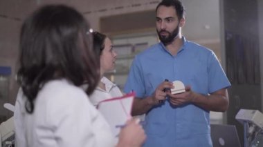Pozitif Orta Doğulu erkek öğretim görevlisinin portresi bir grup öğrenciyle dişçilik hakkında konuşuyor. Beyaz kadınlara stomatoloji öğreten genç bir adam. Kadın asistanlar odontoloji öğreniyor.