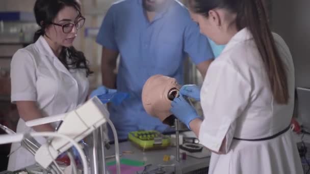 Jeunes belles femmes caucasiennes parler et installer cofferdam sur mannequin. Assistants dentistes confiants concentrés pratiquant. Médecine, stomatologie, dentisterie, odontologie . — Video