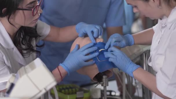 Närbild av kaukasiska kvinnliga tandläkare studenter använder skyltdocka för praktik. Kvinnor som installerar cofferdam på tänder. Utbildning, medicin, odontologi, tandvård. — Stockvideo