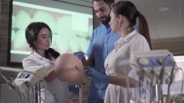 Beau dentiste du Moyen-Orient montrant aux assistants comment travailler avec de l'équipement dans la cavité buccale. Femmes caucasiennes pratiquant la dentisterie avec l'aide d'un stomatologue professionnel. Médecine, cabinet dentaire . — Video