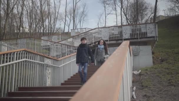 Feliz pareja de estudiantes caucásicos bajando las escaleras en el parque de la ciudad y saliendo. Joven y chica charlando al aire libre yendo de la universidad. Estilo de vida, ocio, citas . — Vídeos de Stock