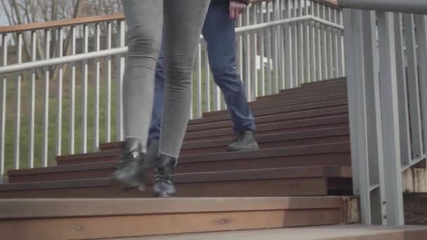 눈에 띄지 않는 소녀와 소년 이 나무 계단을 내려가서 나가고 있다. 수컷 과 암컷의 다리는 화창 한 날 공원에서 뒹굴고 있다. 생활 방식, 여가, 휴식. — 비디오