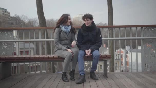 Porträtt av unga kaukasiska man och kvinna sitter på bänk i stadsparken och pratar. Glada tonårsstudenter som dejtar utomhus på höstdagen. Livsstil, kärlek, fritid, romantik. — Stockvideo