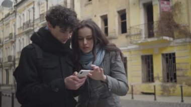 Akıllı telefondan online harita kullanan birkaç beyaz gencin portresi. Kaybolmuş bir çocuk ve kız yabancı bir şehirde dikilip etrafa bakınıyorlar. Turizm, seyahat, yaşam tarzı, yolculuk.