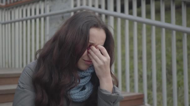 Gros plan de belle fille caucasienne en pleurs. Portrait d'une jeune femme brune malheureuse aux yeux noisette assise dans un escalier du parc. Dépression, solitude, stress, mode de vie . — Video