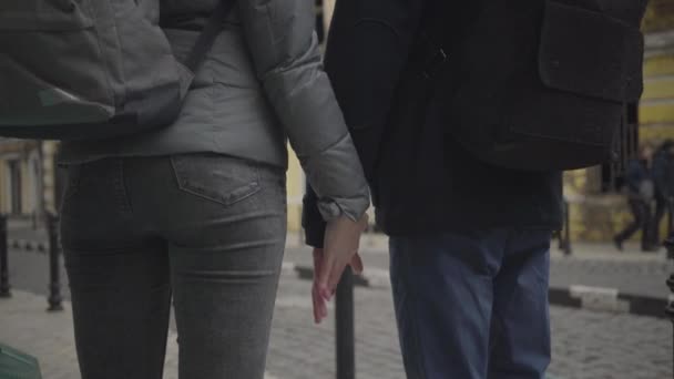 Ung vit man och kvinna tar varandras händer och går iväg längs stadens gata. Pojkvän och flickvän med ryggsäckar som dejtar i stan. Ungdom, romantik, kärlek, livsstil. — Stockvideo