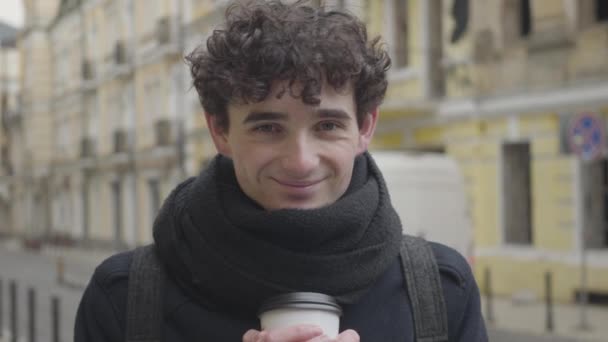 Zbliżenie młodego białego mężczyzny mrugającego i uśmiechającego się do kamery. Portret Brunetki z kręconymi włosami i siwymi oczami na ulicy. Styl życia, szczęście, wypoczynek. — Wideo stockowe