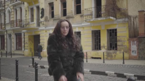 Portrait of joyful stylish girl in fur coat and sunglasses having fun on city street. Cheerful young woman dancing, spinning and jumping in foreign town. Tourism, leisure, fun, lifestyle. — Stock Video