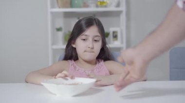 Tiksinmiş Orta Doğulu bir kızın portresi tabakta lapayla iğrenç görünüyor. Siyah saçlı ve kahverengi gözlü küçük çocuk sabah sağlıklı bir kahvaltı yapıyor. Beslenme, çocukluk, beslenme.