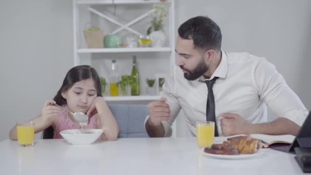 Spěchající obchodník ze Středního východu mluví s malou dívkou, která jí snídani a ukazuje na hodinky. Otec žádá dceru, aby si pospíšila. Nudné dítě bez chuti k jídlu. Rodinný vztah, životní styl. — Stock video