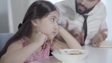Bulanık Orta Doğulu genç adam, küçük üzgün kıza bağırıyor, lapayı kaşıkla karıştırıyor. Sabah itaatsiz kızıyla tartışan aceleci bir babanın portresi. Yaşam tarzı, kahvaltı, ebeveynlik..