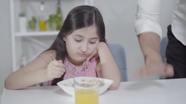 Onherkenbare vader die emotioneel gebaart en laat gebaar maakt als klein meisje zonder eetlust havermout in het bord te mengen. Dochter ontbijt met gehaaste zakenman. Levensstijl. — Stockvideo