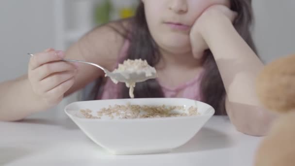 Unalmas, felismerhetetlen kislány, aki gabonapelyhet kevert kanállal. Boldogtalan közel-keleti gyerek reggelizik reggel. Életmód, unalom, szomorúság, egészséges táplálkozás. — Stock videók